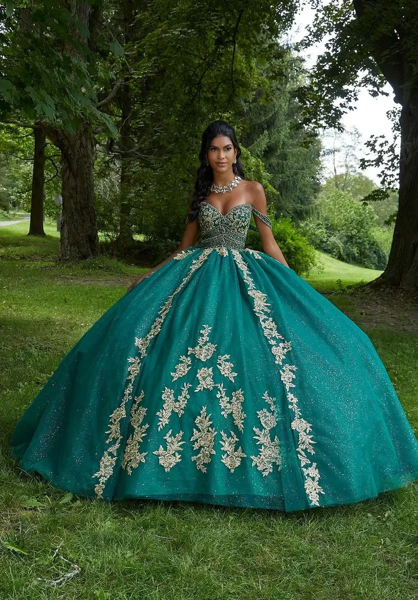 Model is wearing a strapless rhinestone quinceanera gown with off the shoulder sleeves and a sheer boned bodice