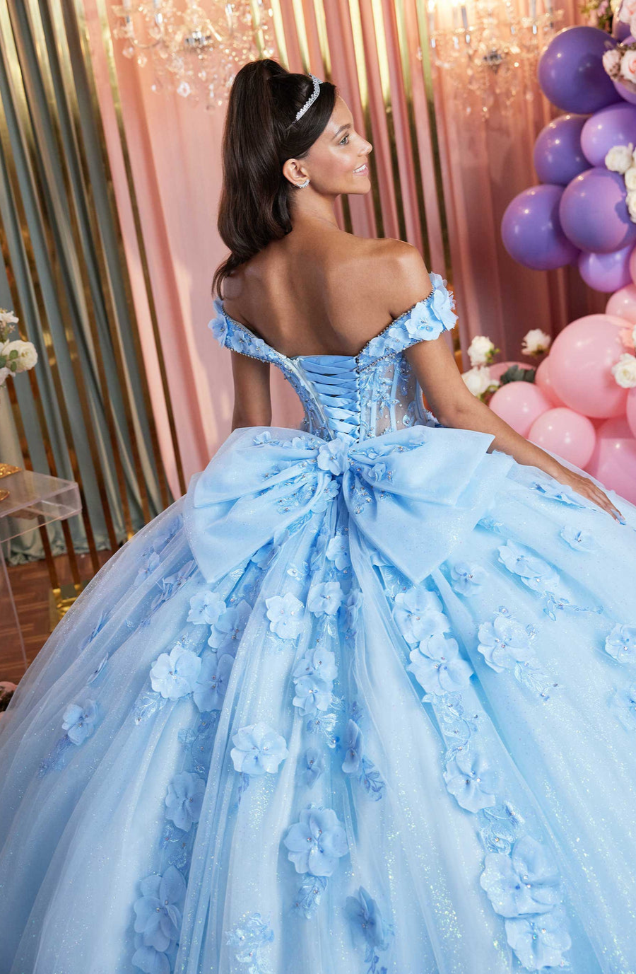 Model is wearing an off the shoulder light blue quinceanera dress with a large bow on the back