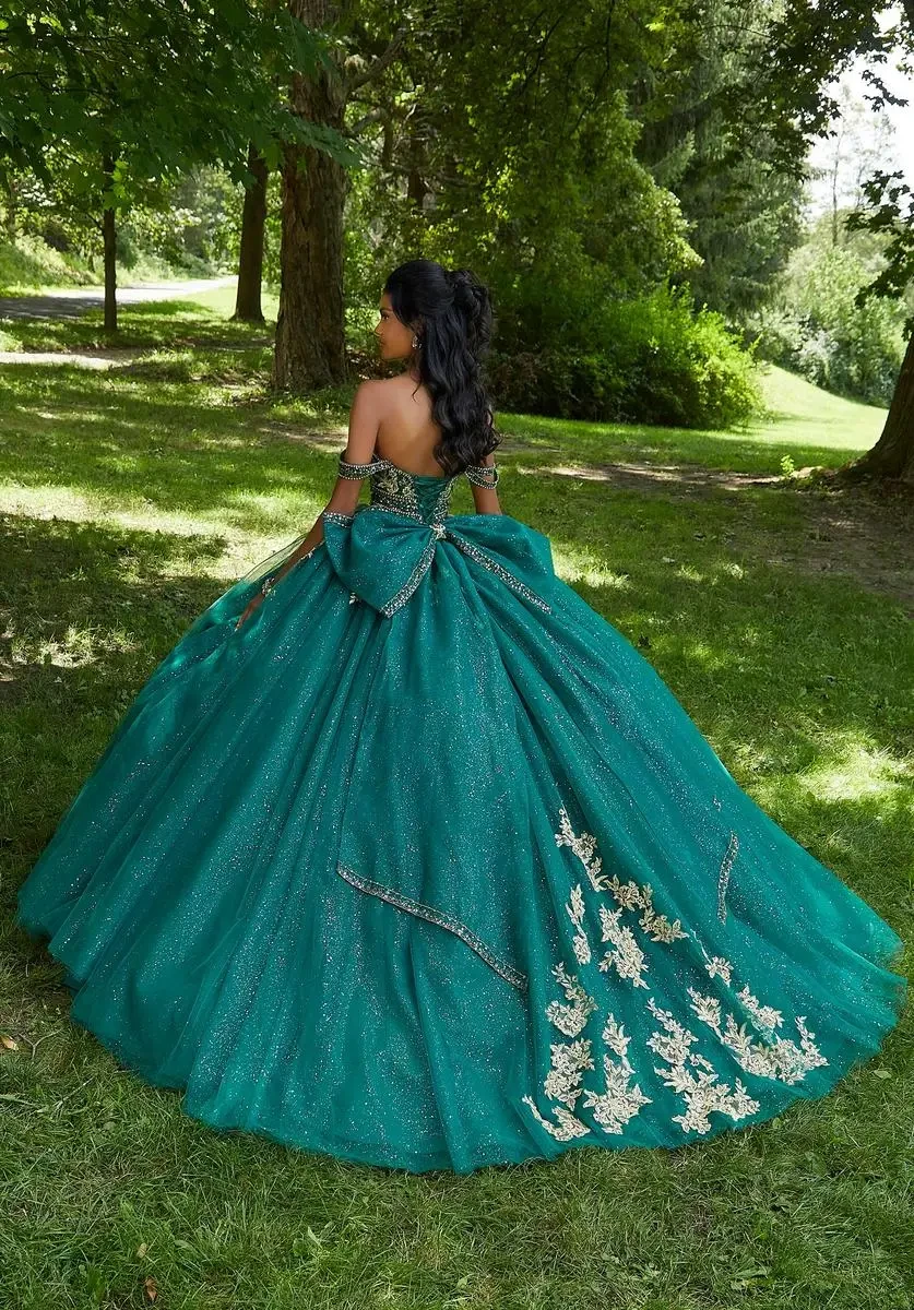 Model is wearing a strapless rhinestone quinceanera gown with off the shoulder sleeves and a sheer boned bodice