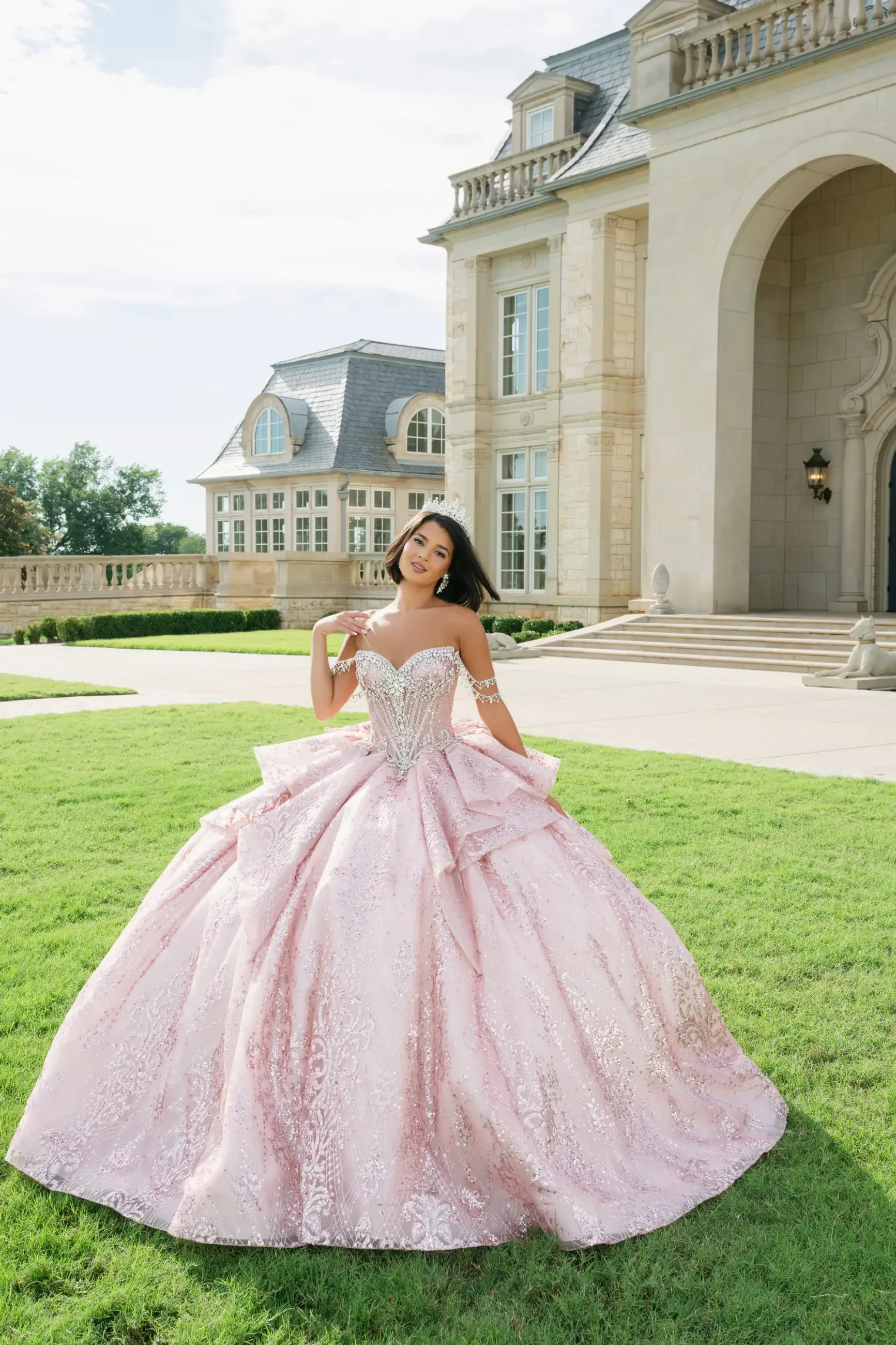 A woman in an elegant pink ball gown stands on a lush lawn in front of a grand mansion. She smiles confidently, conveying elegance and joy.