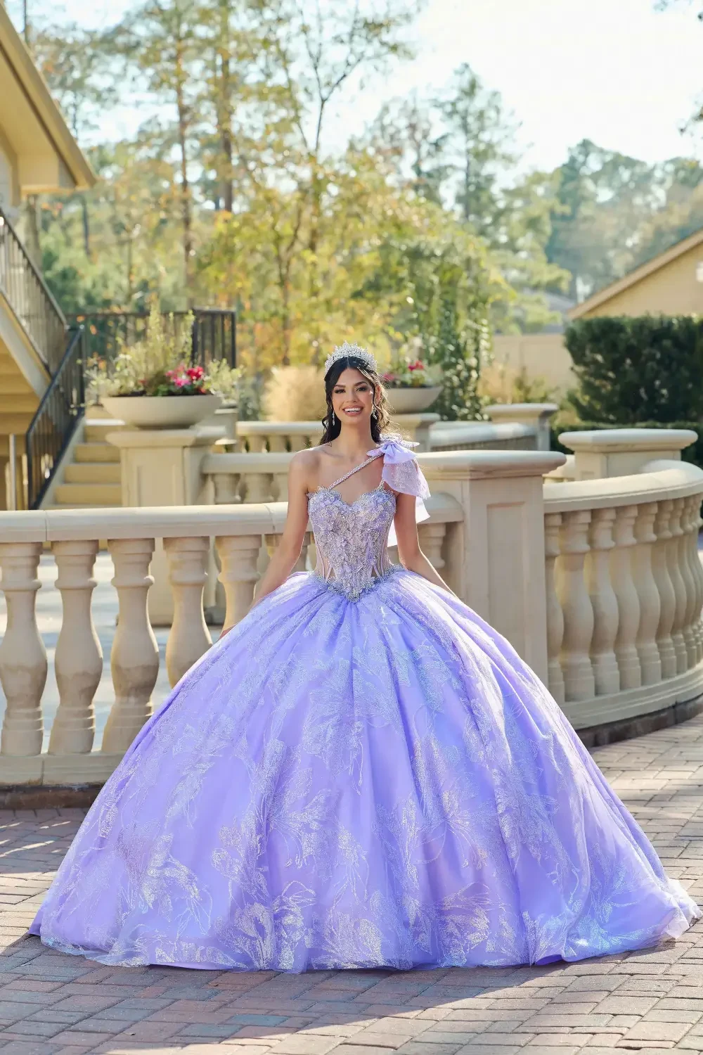 A young woman in a lavender ball gown with intricate beading and a one-shoulder design, standing outdoors in a garden setting.