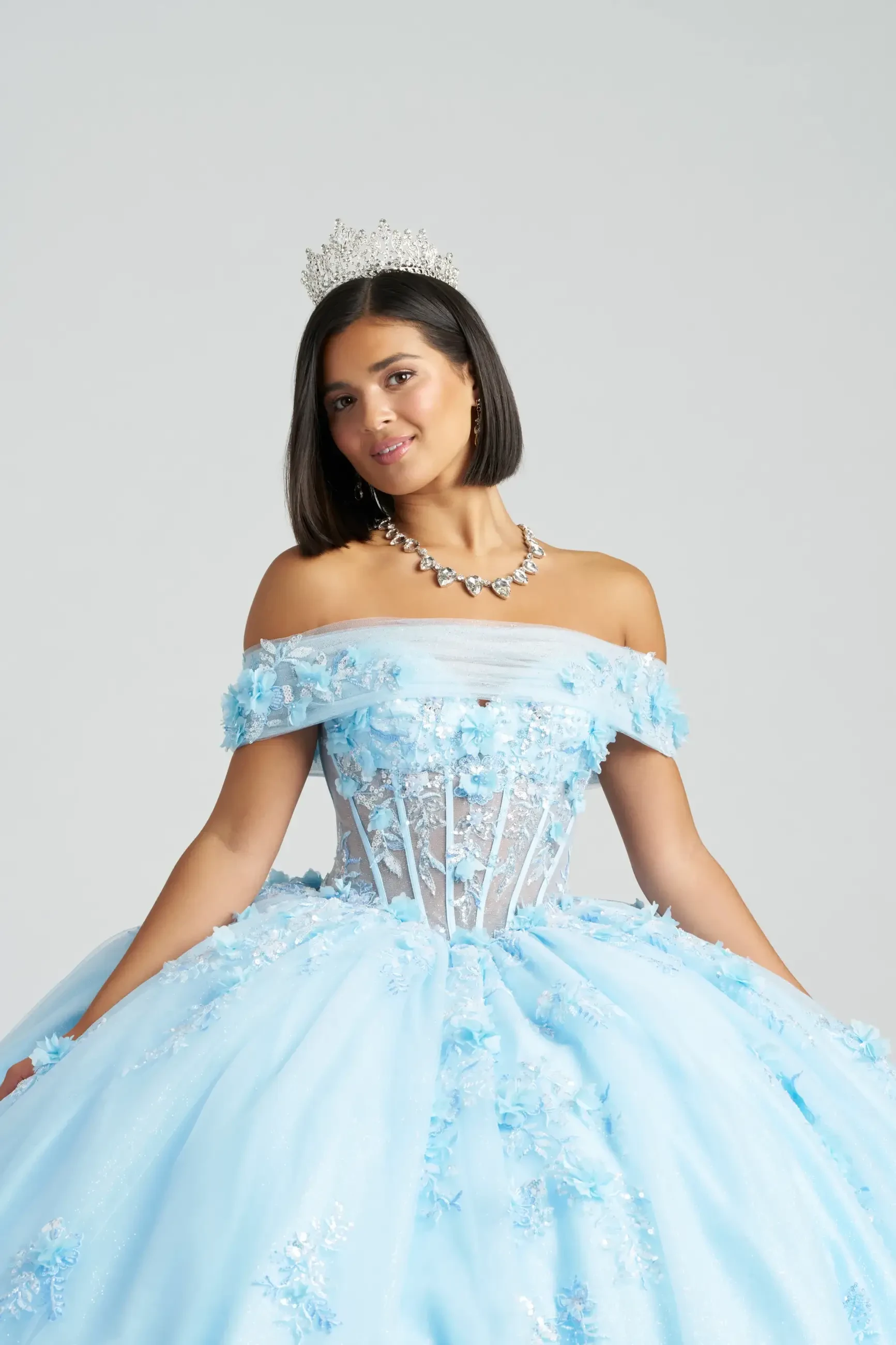 A woman wearing a stunning light blue ball gown with off-the-shoulder sleeves and intricate embellishments, alongside a tiara.